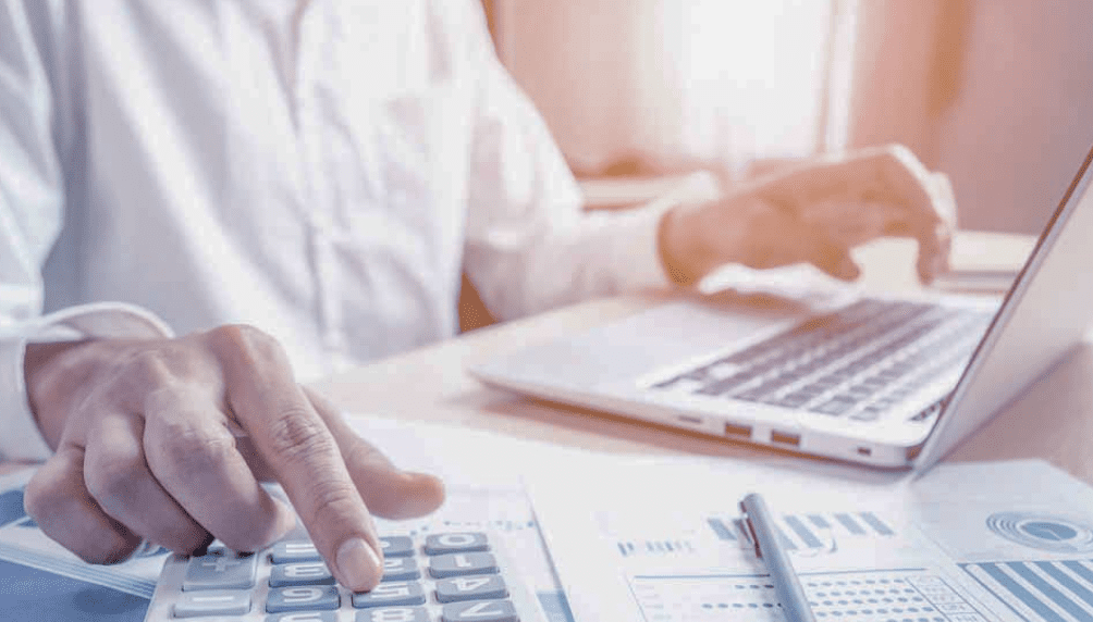Person calculating finances with calculator and laptop