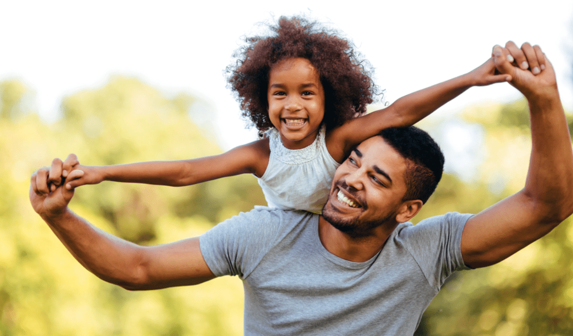 Smiling man gives child piggyback ride outdoors