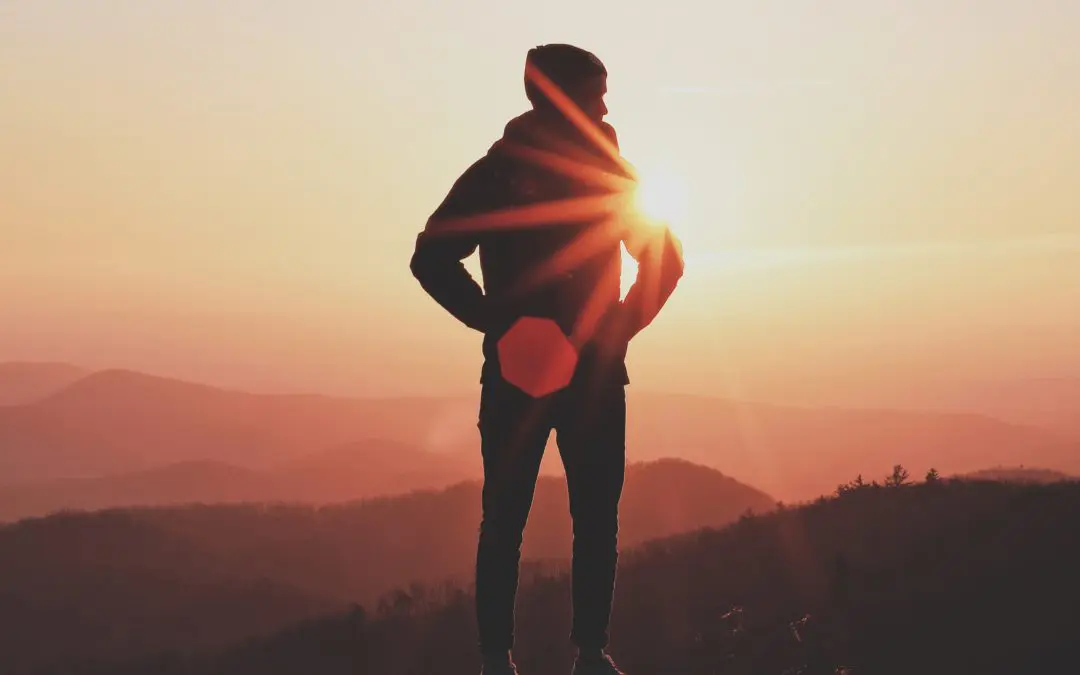 Silhouette of person standing at mountain sunset