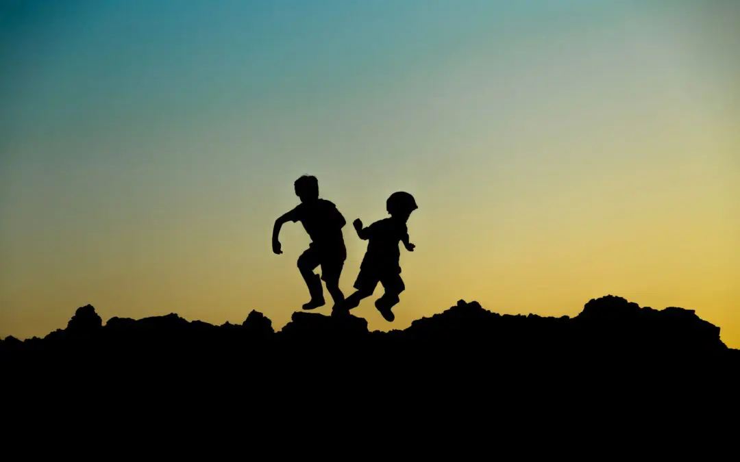 Silhouettes of two children jumping at sunset