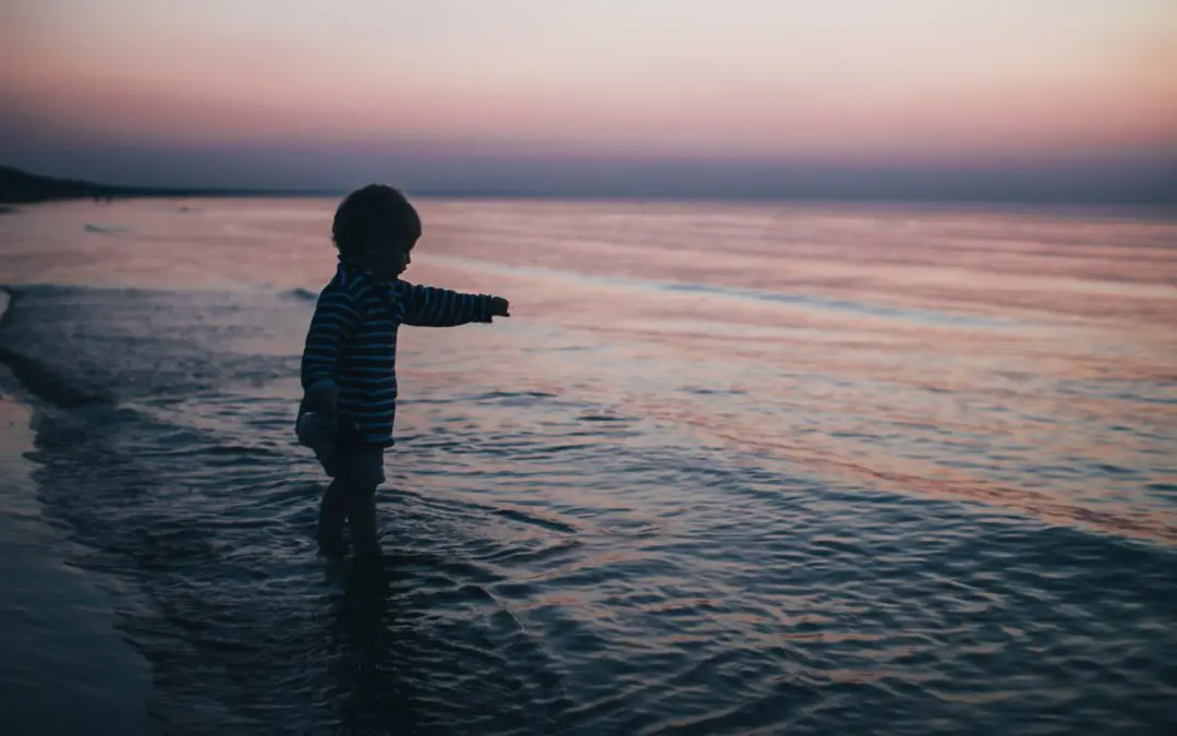 Child silhouetted in ocean at sunset