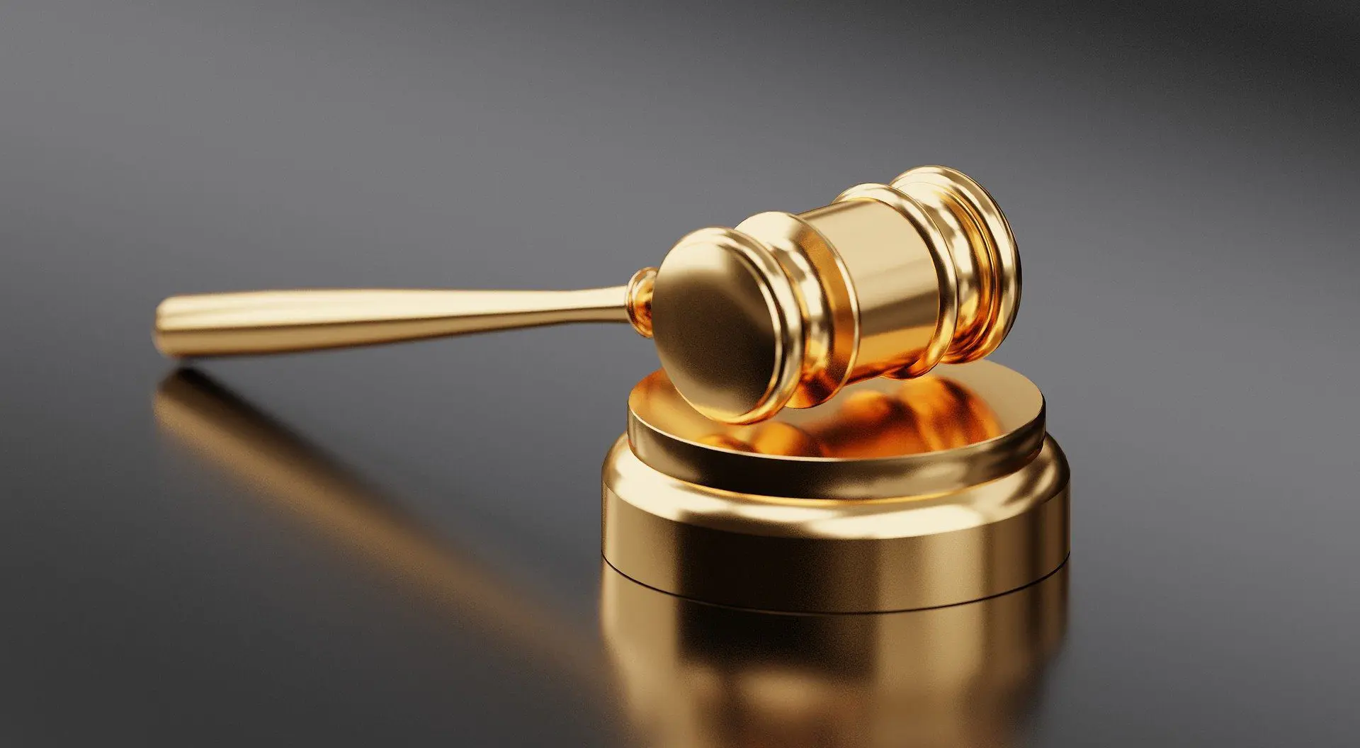 Gold judge gavel on reflective surface