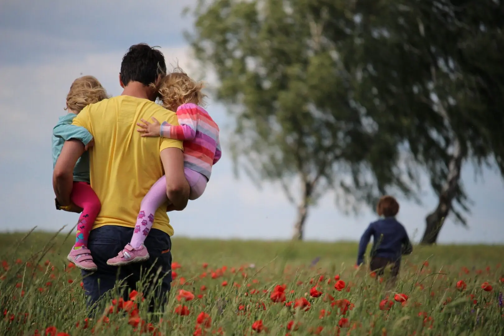 Parent carrying two children in poppy field