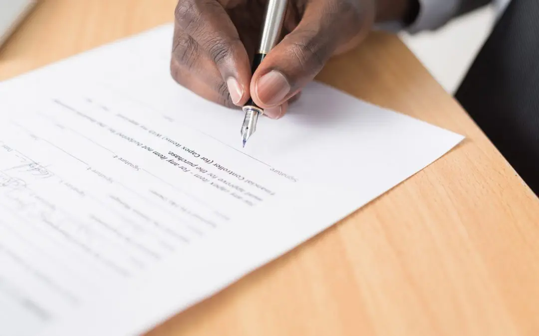 Hand signing a document on wooden desk