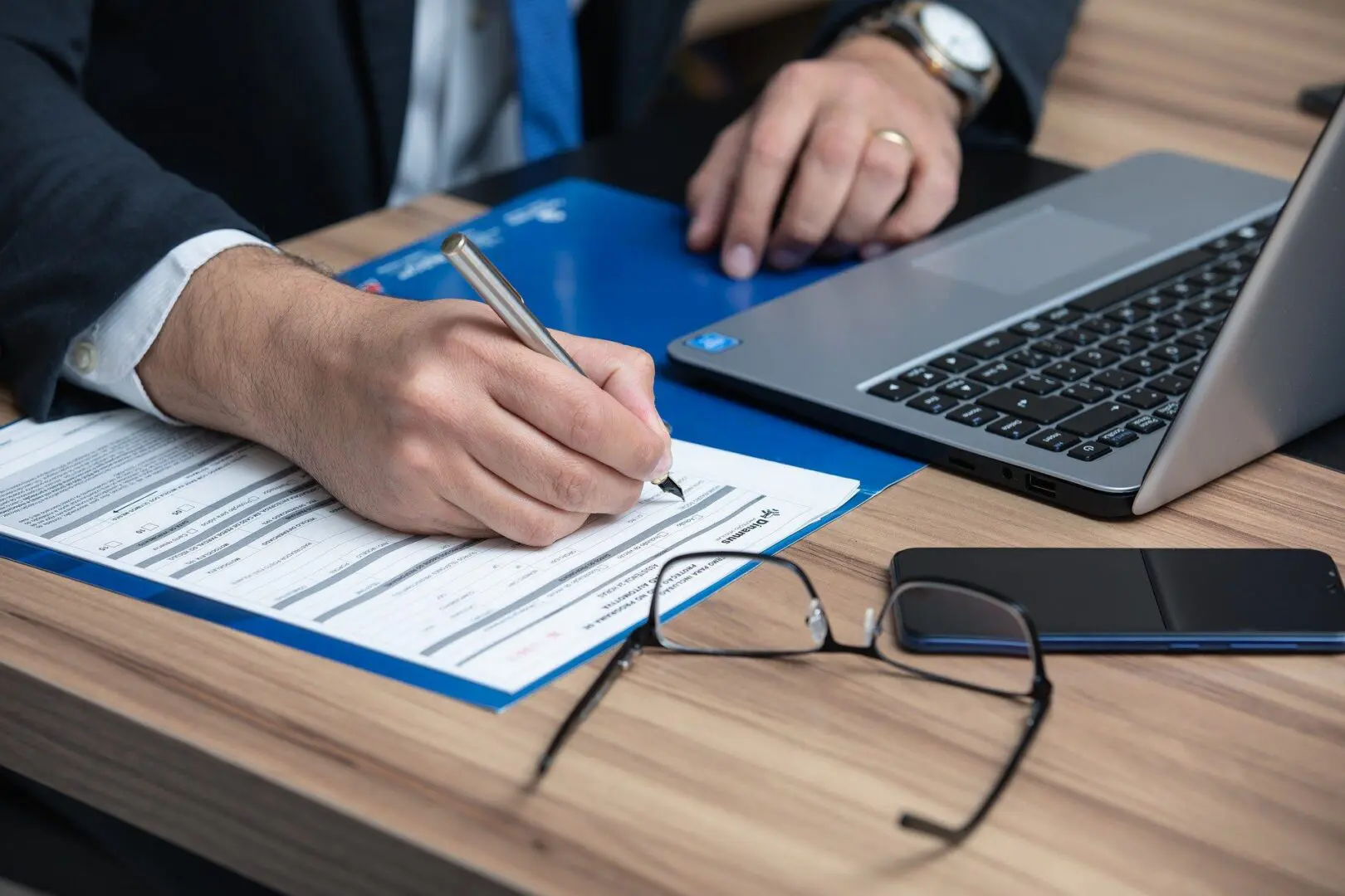 Person signing form at desk with laptop