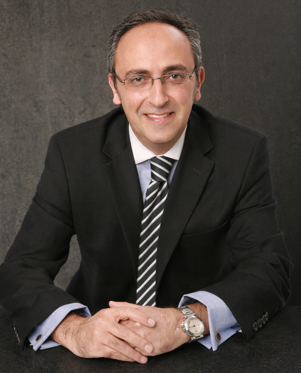 Professional man in suit sitting with hands clasped, smiling.