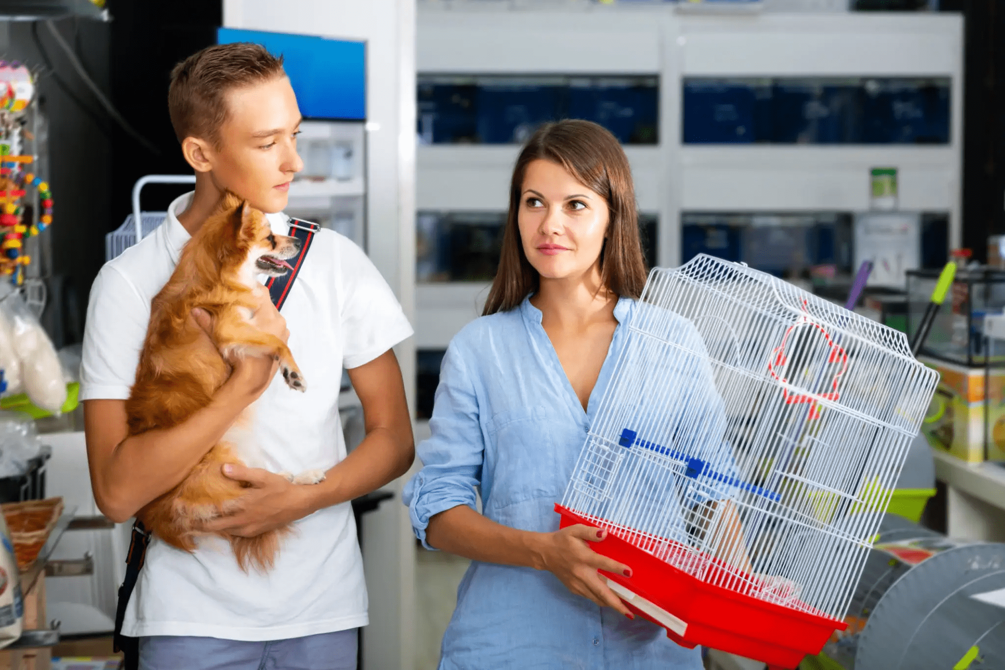 Couple holding dog and birdcage in store.
